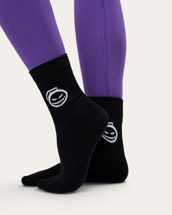 Calzini sportivi Bombafit neri con grafica di zucca stilizzata bianca, indossati con leggings viola