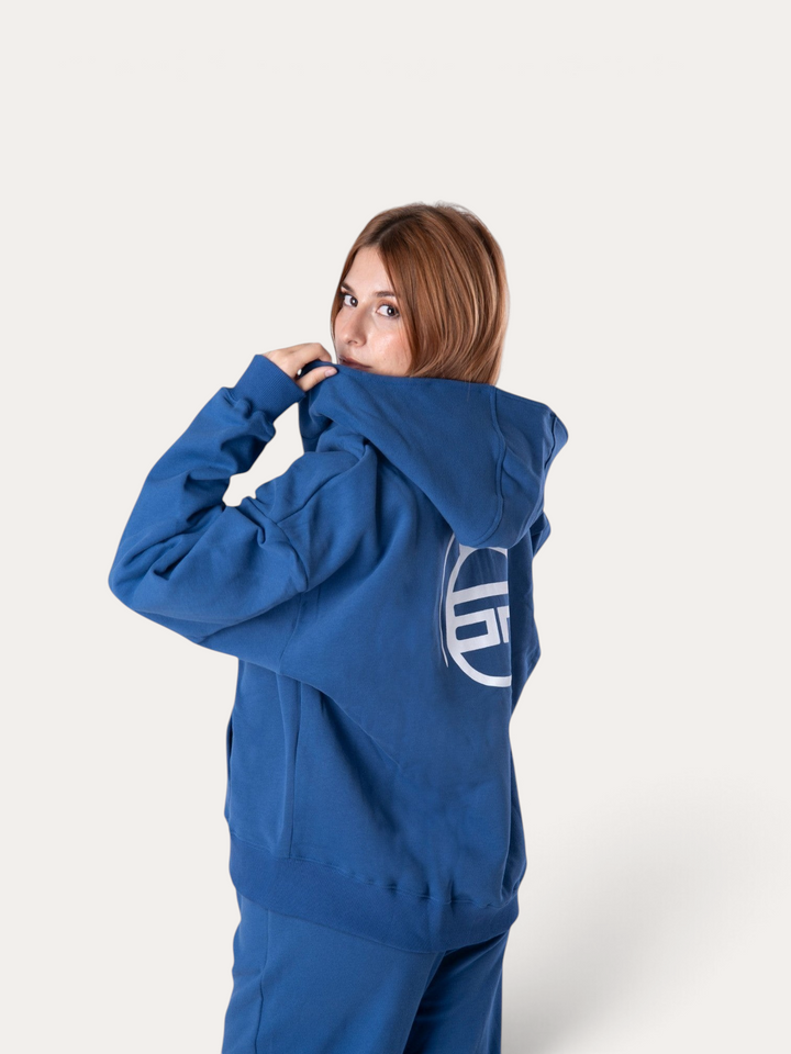 Modella indossa la felpa con cappuccio Flux Hoodie blu reale di Bombafit con logo circolare bianco sul retro