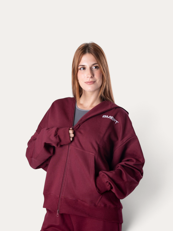 Modella indossa una felpa con cappuccio Bombafit Flux color bordeaux con zip frontale e logo sul petto