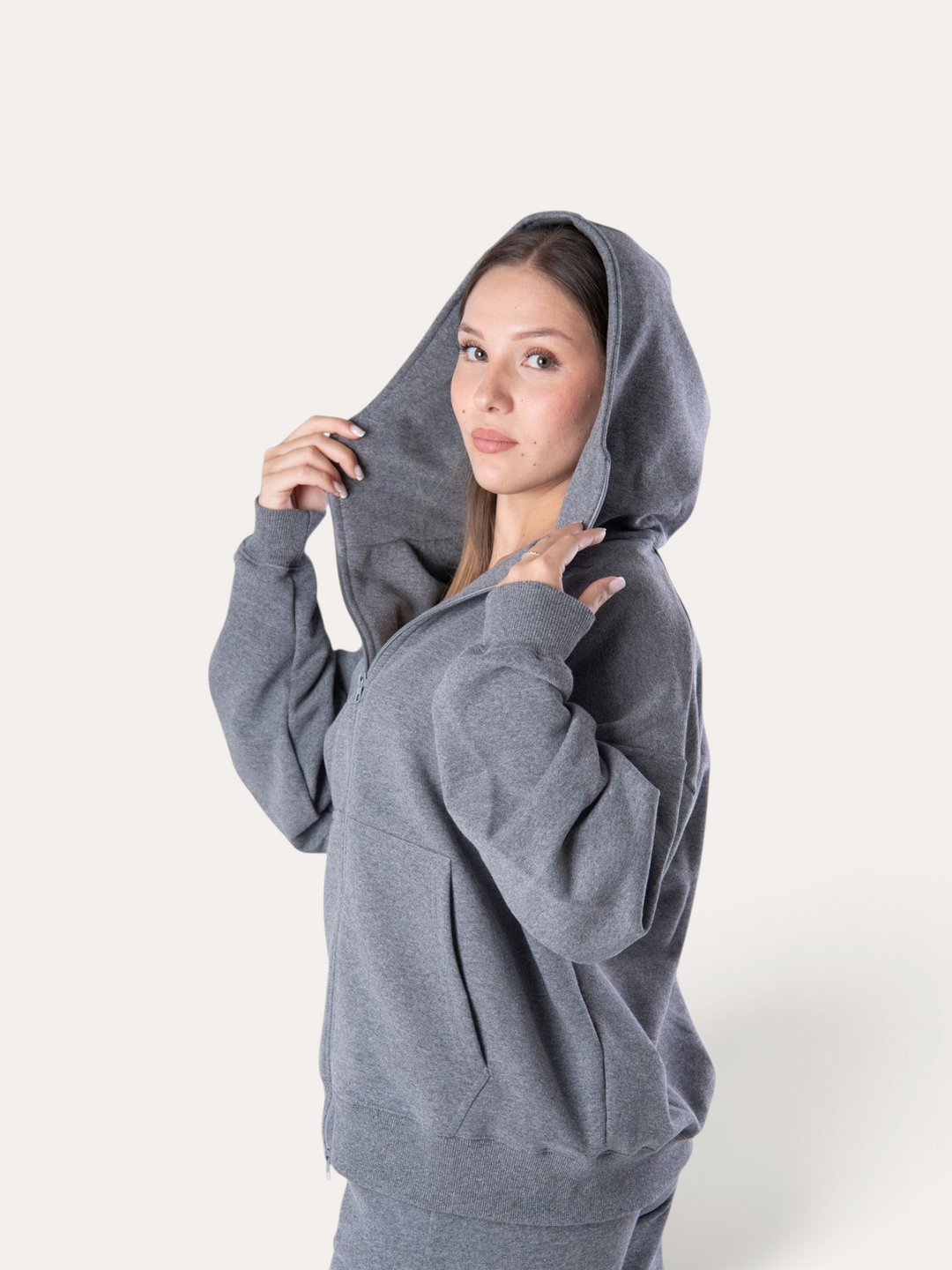 Modella indossa una felpa con cappuccio Bombafit Flux grigio melange con zip frontale e vestibilità ampia