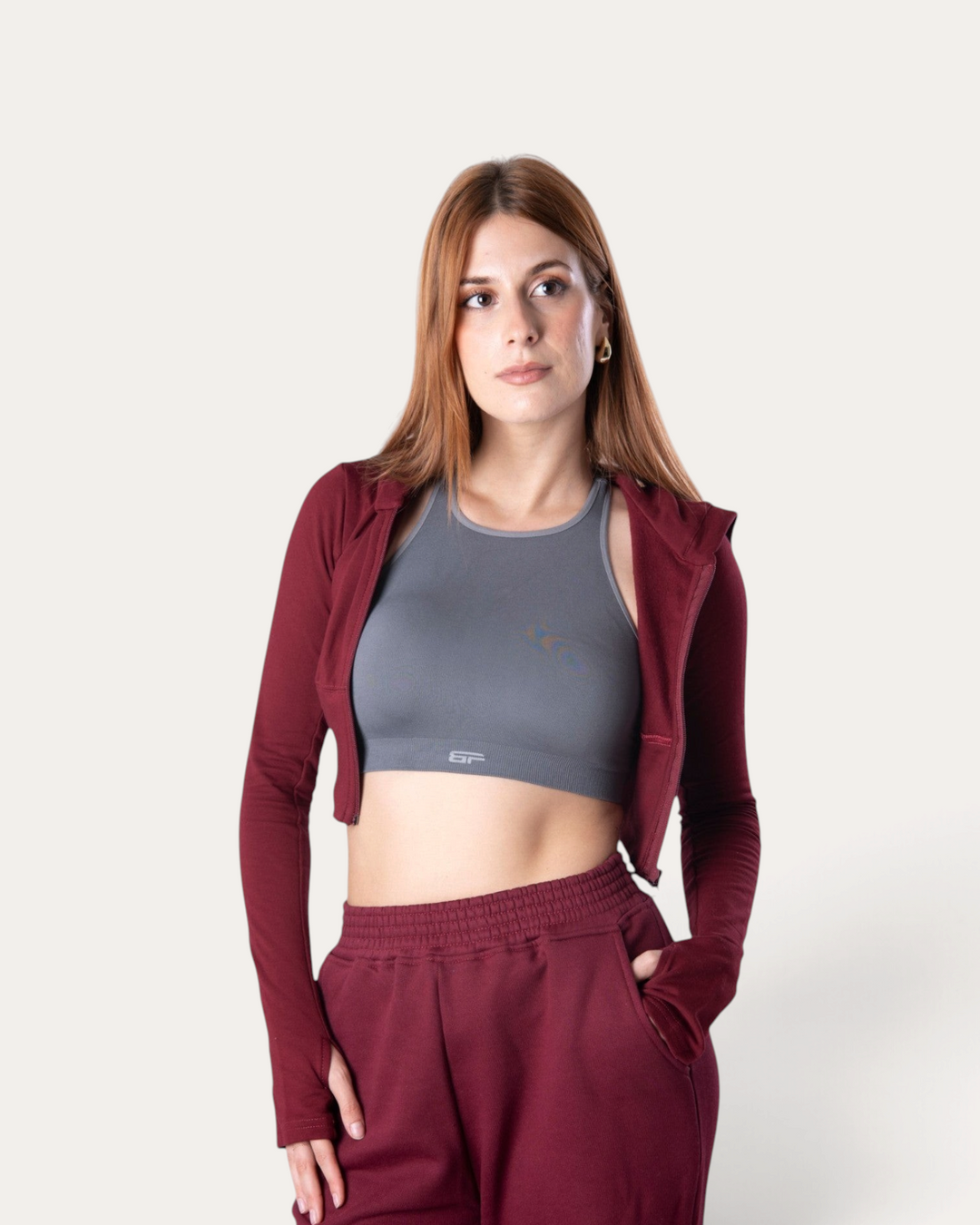 Modella indossa la felpa corta con zip Bombafit Flux Mini color bordeaux abbinata a pantaloni sportivi coordinati