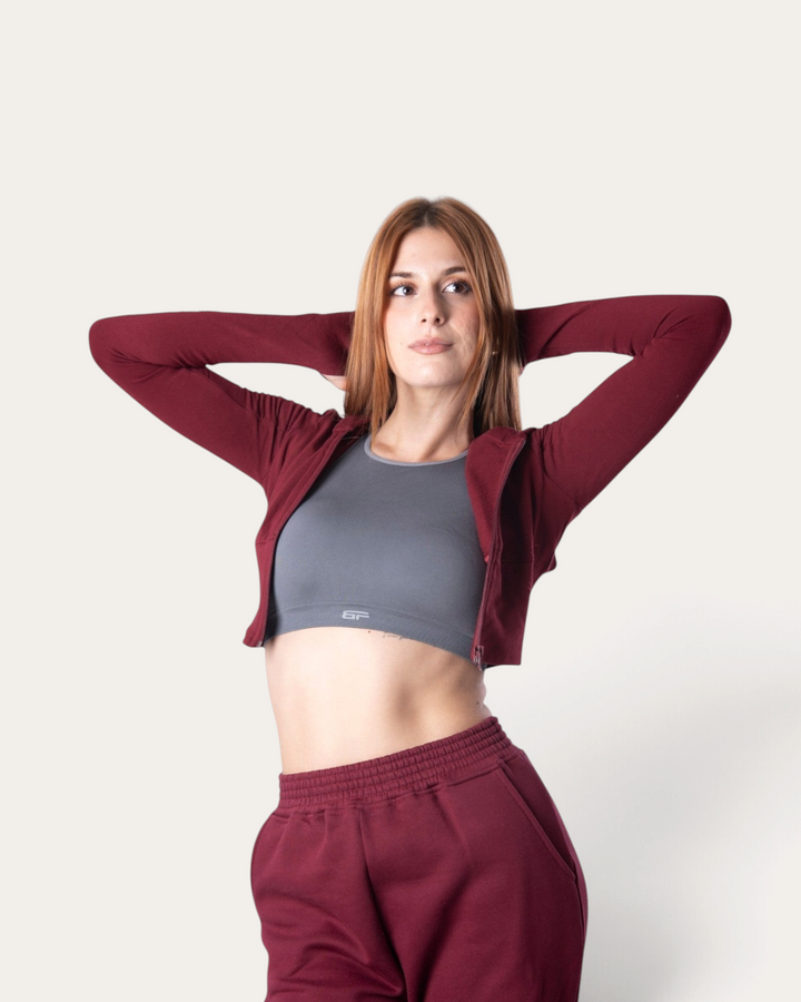 Modella indossa una felpa corta Bombafit color bordeaux con zip, abbinata a pantaloni sportivi coordinati