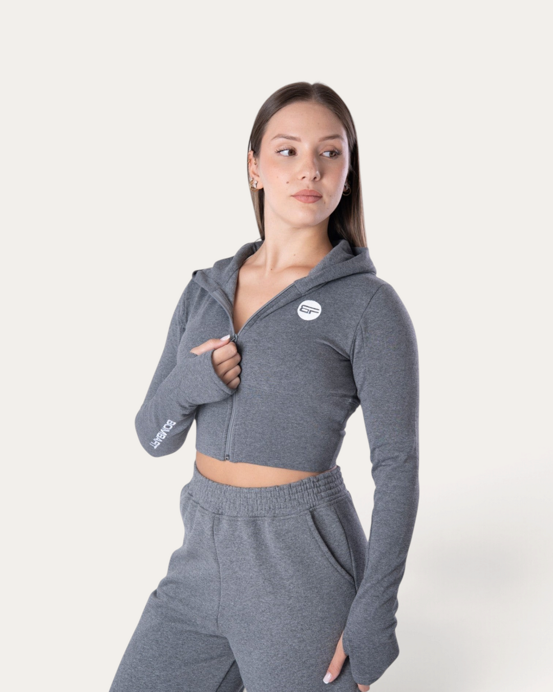 Modella indossa la felpa corta Bombafit Flux Mini grigio melange con zip, cappuccio e fori per i pollici