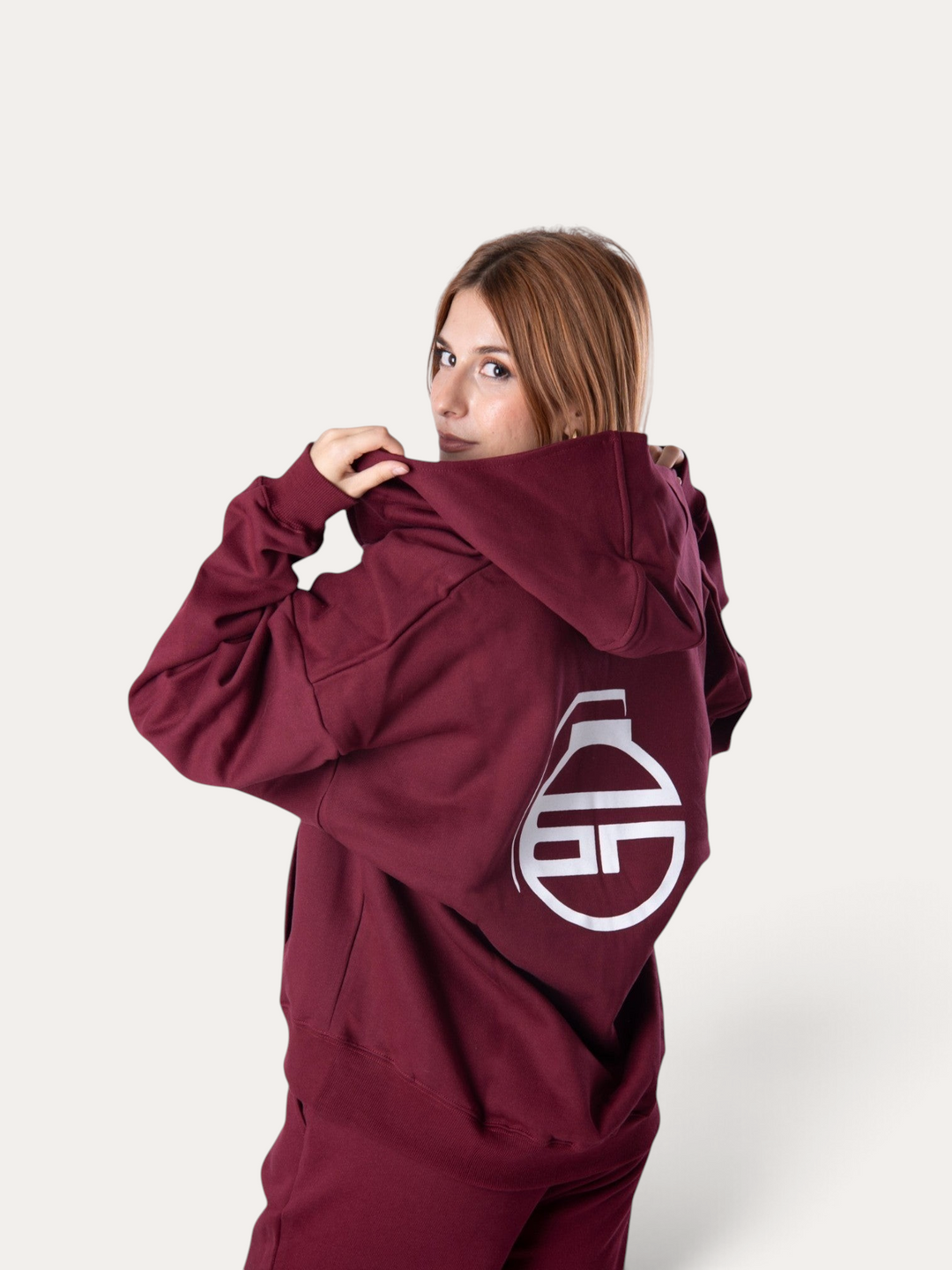 Donna che indossa la felpa con cappuccio Bombafit Flux color bordeaux con logo bianco stampato sul retro