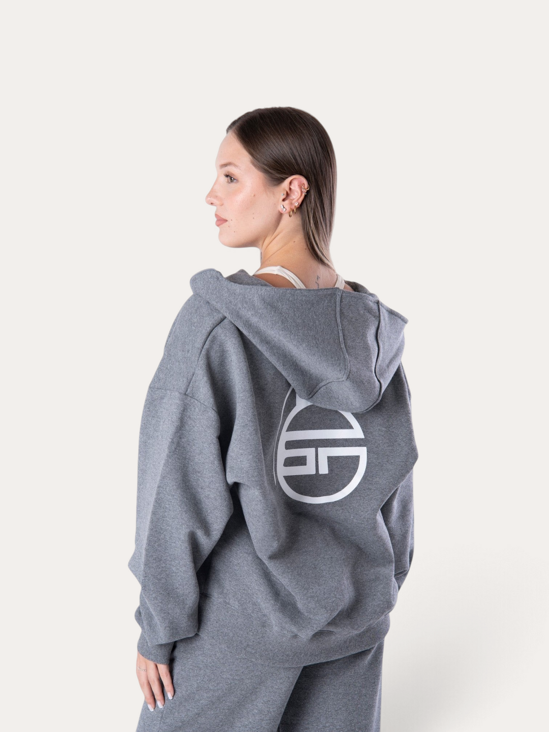 Modella indossa la felpa con cappuccio Bombafit Flux grigio melange con logo circolare bianco sul retro