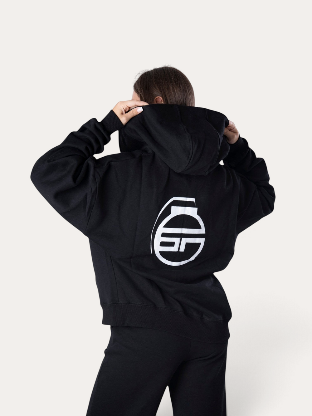 Modella indossa la felpa con cappuccio nera Flux Hoodie di Bombafit con logo bianco stampato sul retro