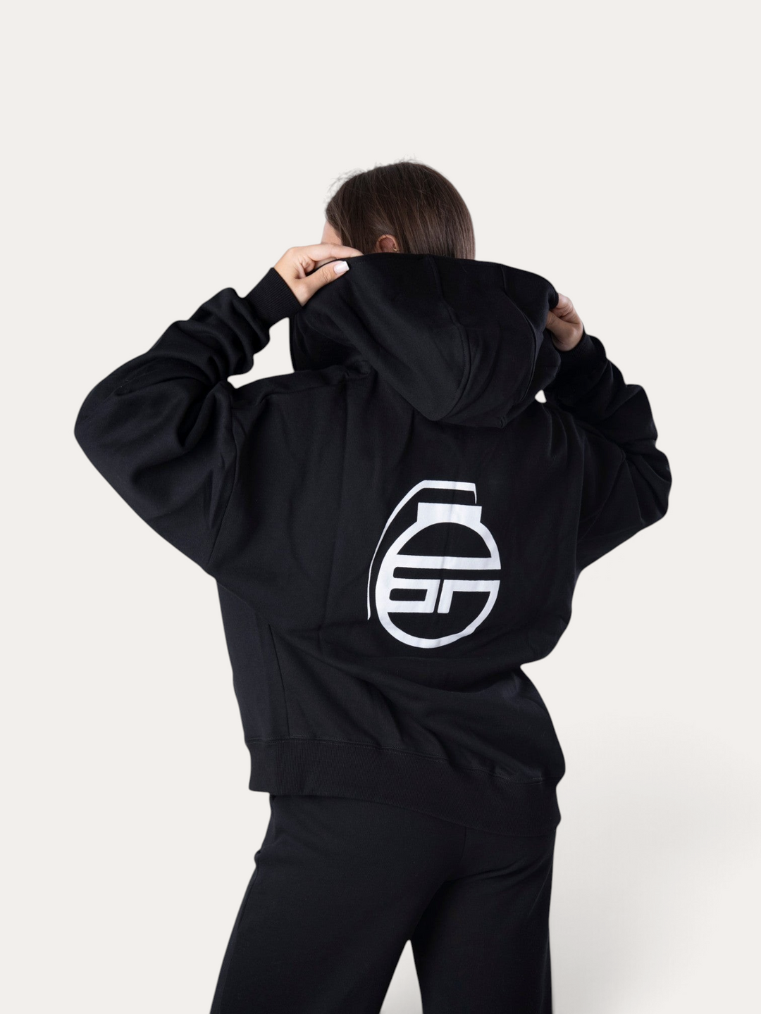 Modella indossa la felpa con cappuccio nera Flux Hoodie di Bombafit con logo bianco stampato sul retro