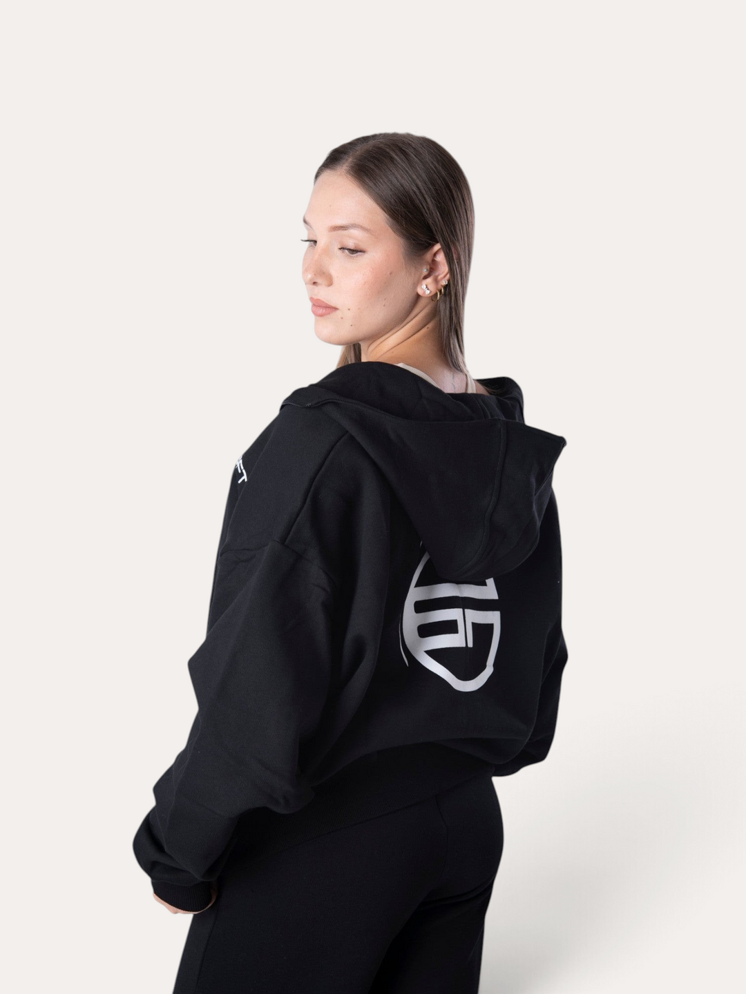 Modella indossa la felpa nera Flux Hoodie di Bombafit con cappuccio e logo bianco stampato sul retro