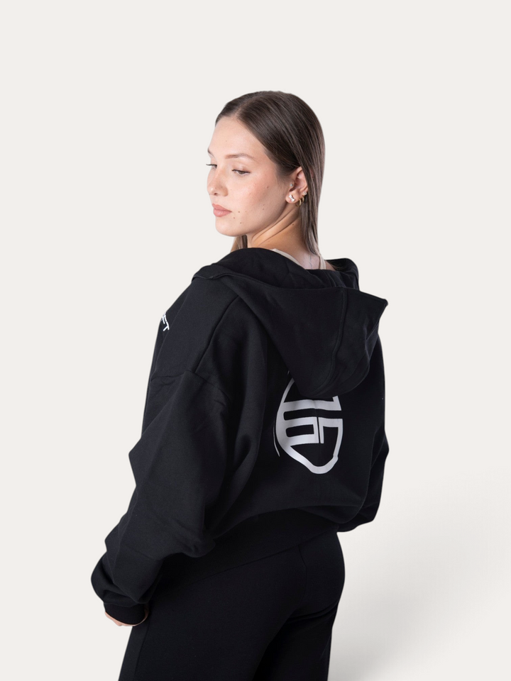 Modella indossa la felpa nera Flux Hoodie di Bombafit con cappuccio e logo bianco stampato sul retro