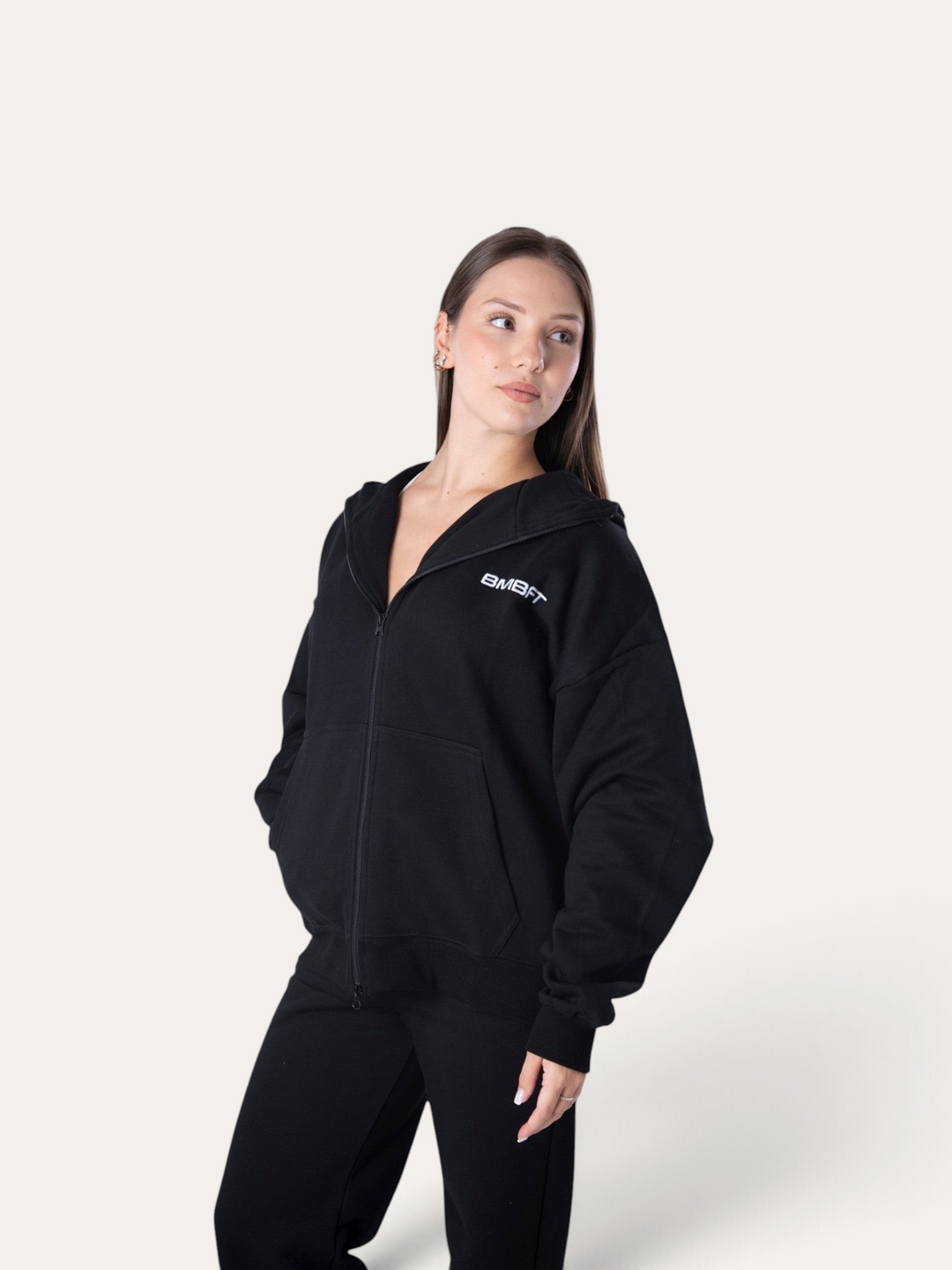 Modella indossa la felpa con cappuccio e zip Flux Hoodie nera di Bombafit con logo bianco sul petto