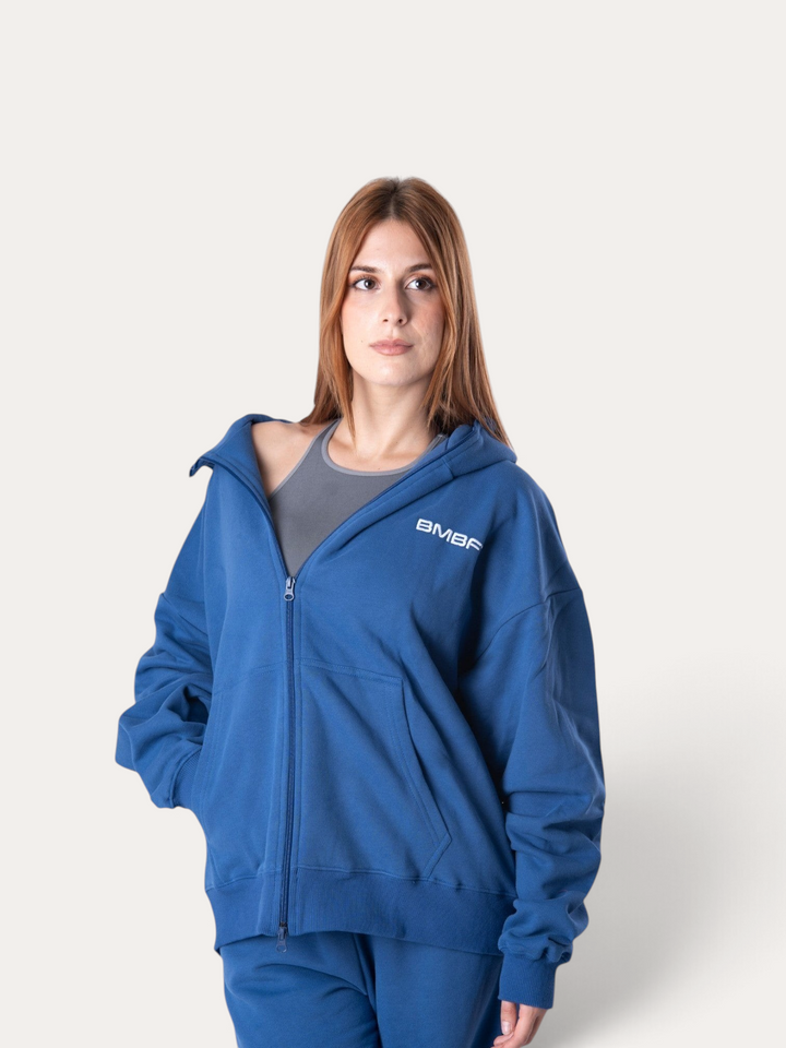 Modella indossa una felpa con cappuccio e zip Bombafit blu reale con logo bianco sul petto