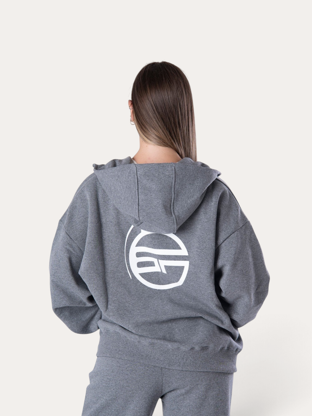 Donna di spalle indossa la felpa con cappuccio Bombafit Flux grigio melange con logo bianco stampato sul retro
