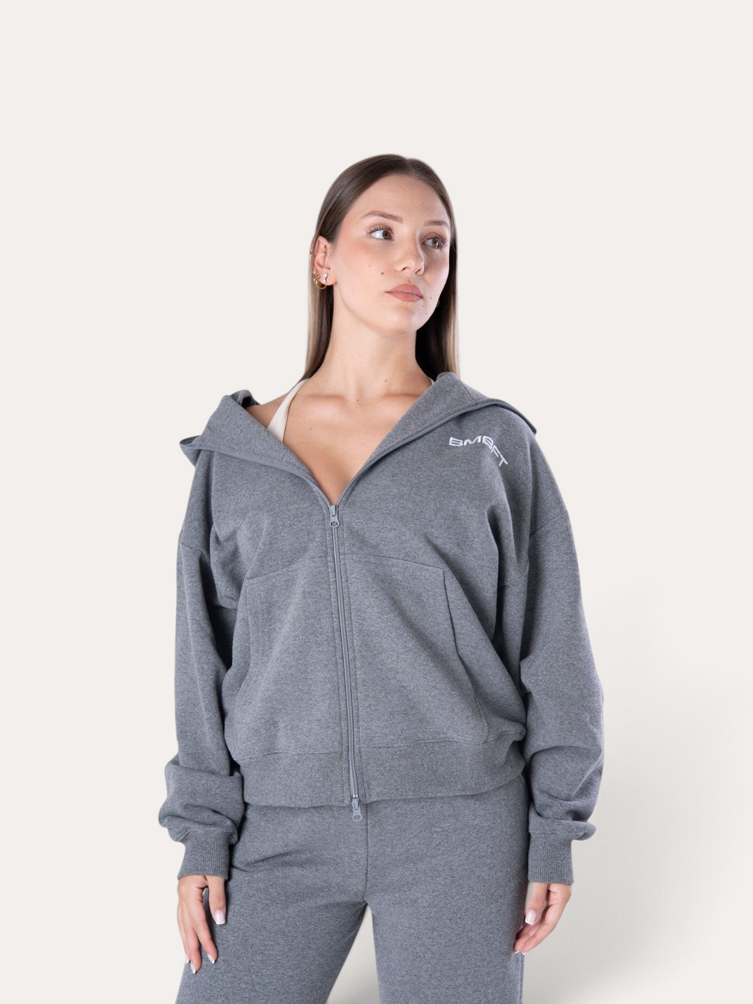 Modella indossa la felpa con cappuccio Flux Hoodie Bombafit grigio melange con zip frontale e logo ricamato