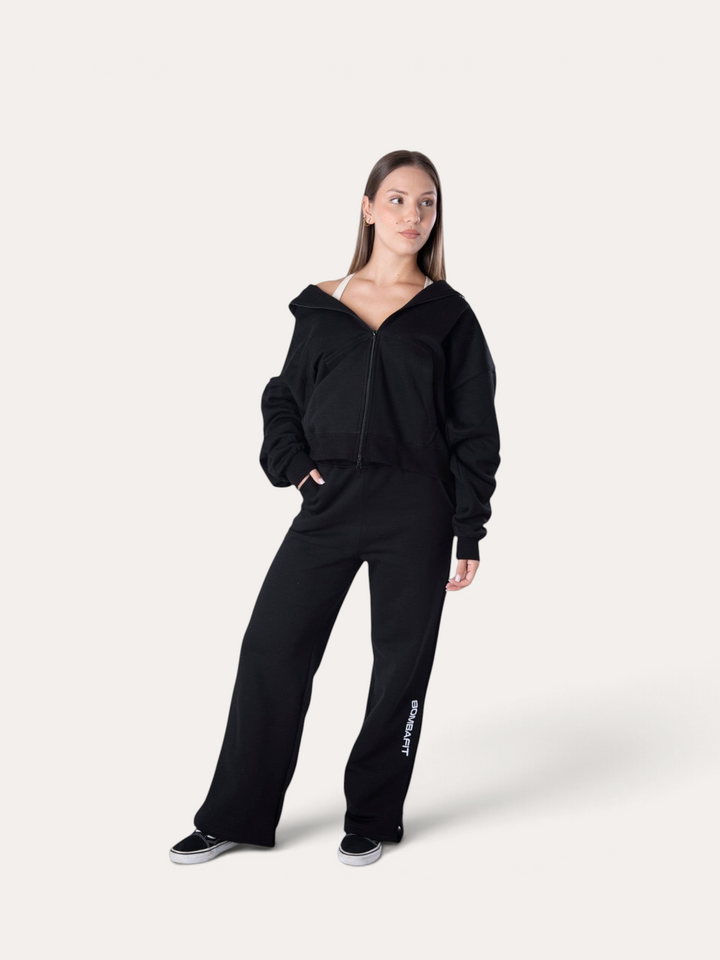 Modella indossa la Bombafit Flux Hoodie nera con zip, abbinata a pantaloni sportivi coordinati su sfondo neutro.