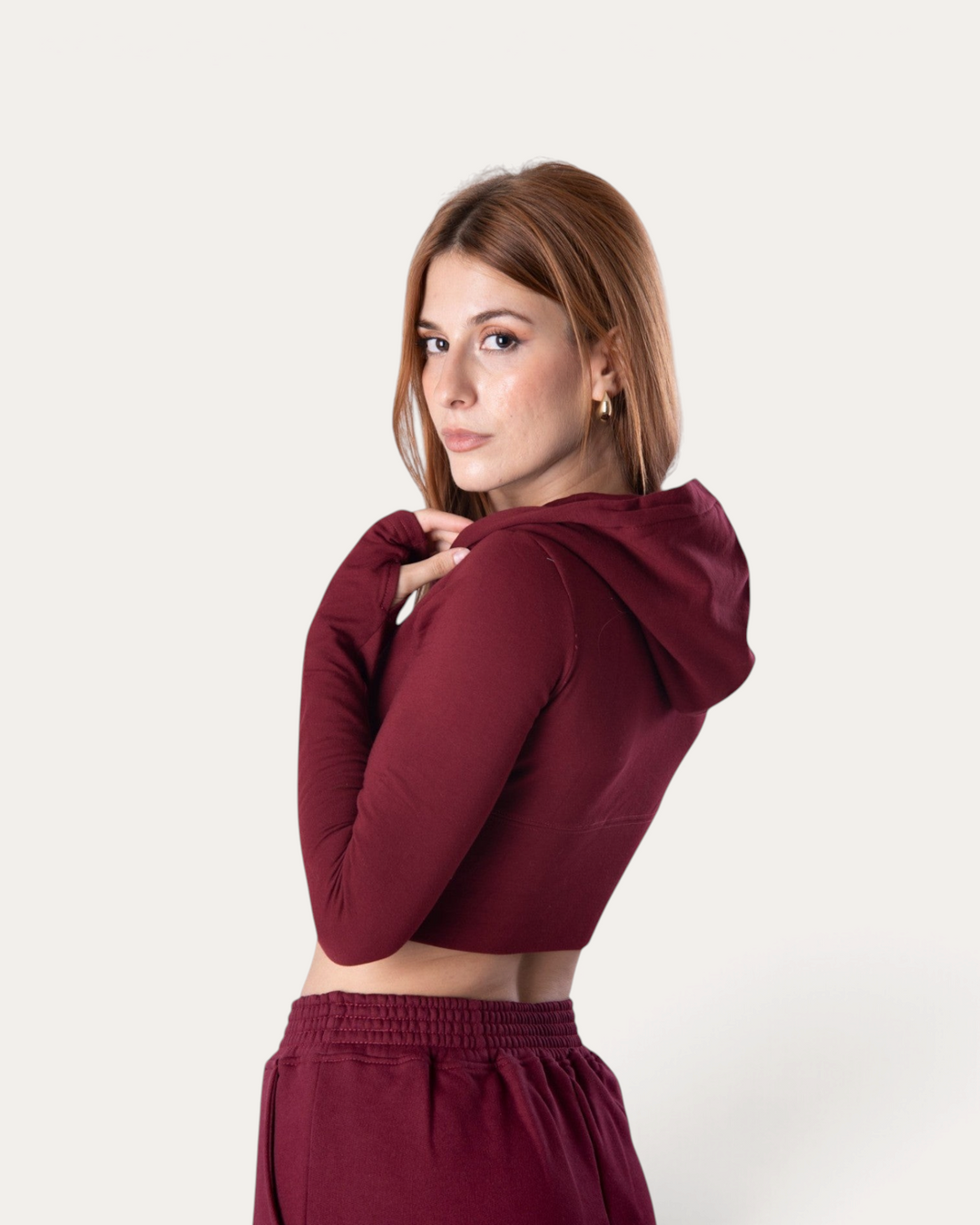 Modella indossa la felpa corta Bombafit Flux Mini Hoodie color bordeaux con cappuccio e maniche lunghe