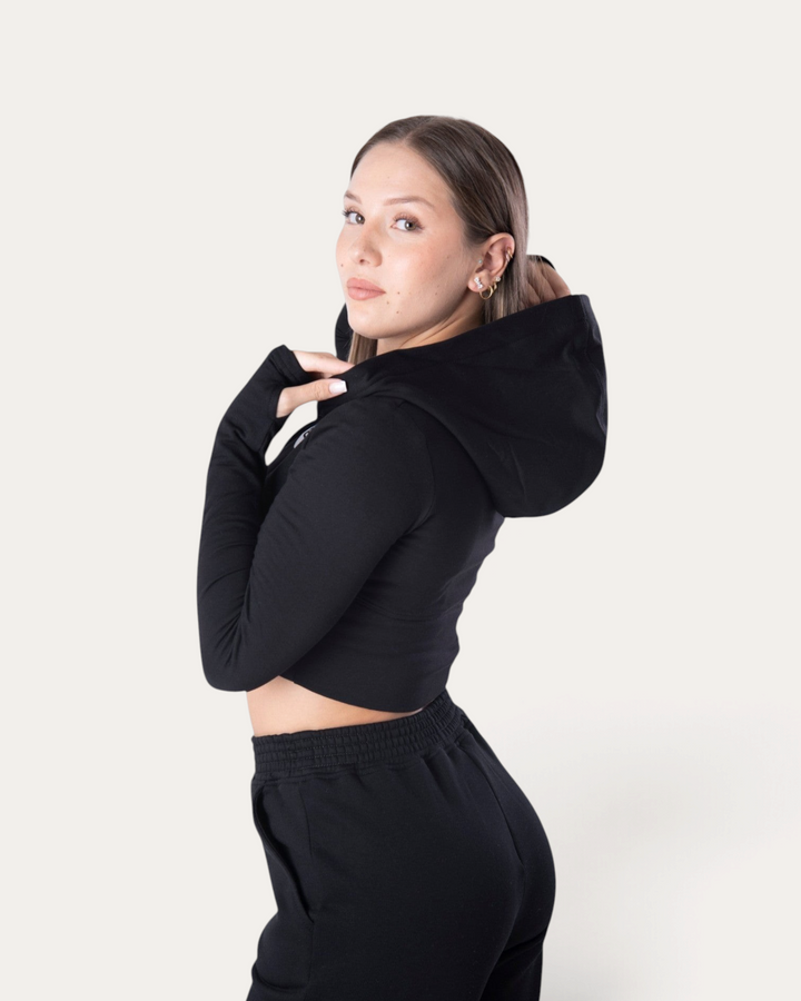 Modella indossa la felpa corta nera Bombafit Flux Mini con cappuccio e fori per i pollici, vista laterale
