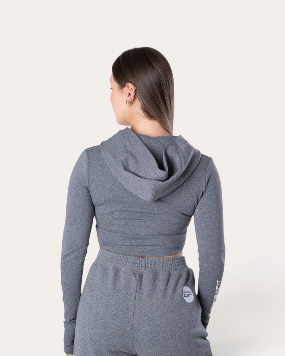 Vista posteriore di una modella che indossa la felpa corta Bombafit Flux Mini Hoodie in grigio melange