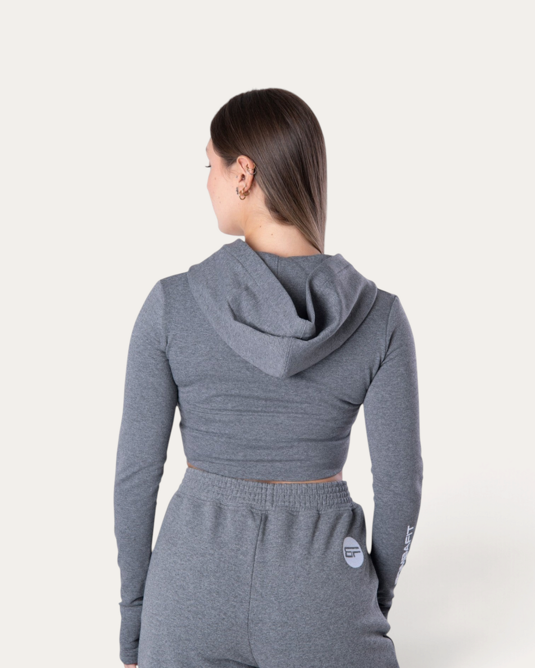 Vista posteriore di una modella che indossa la felpa corta Bombafit Flux Mini Hoodie in grigio melange