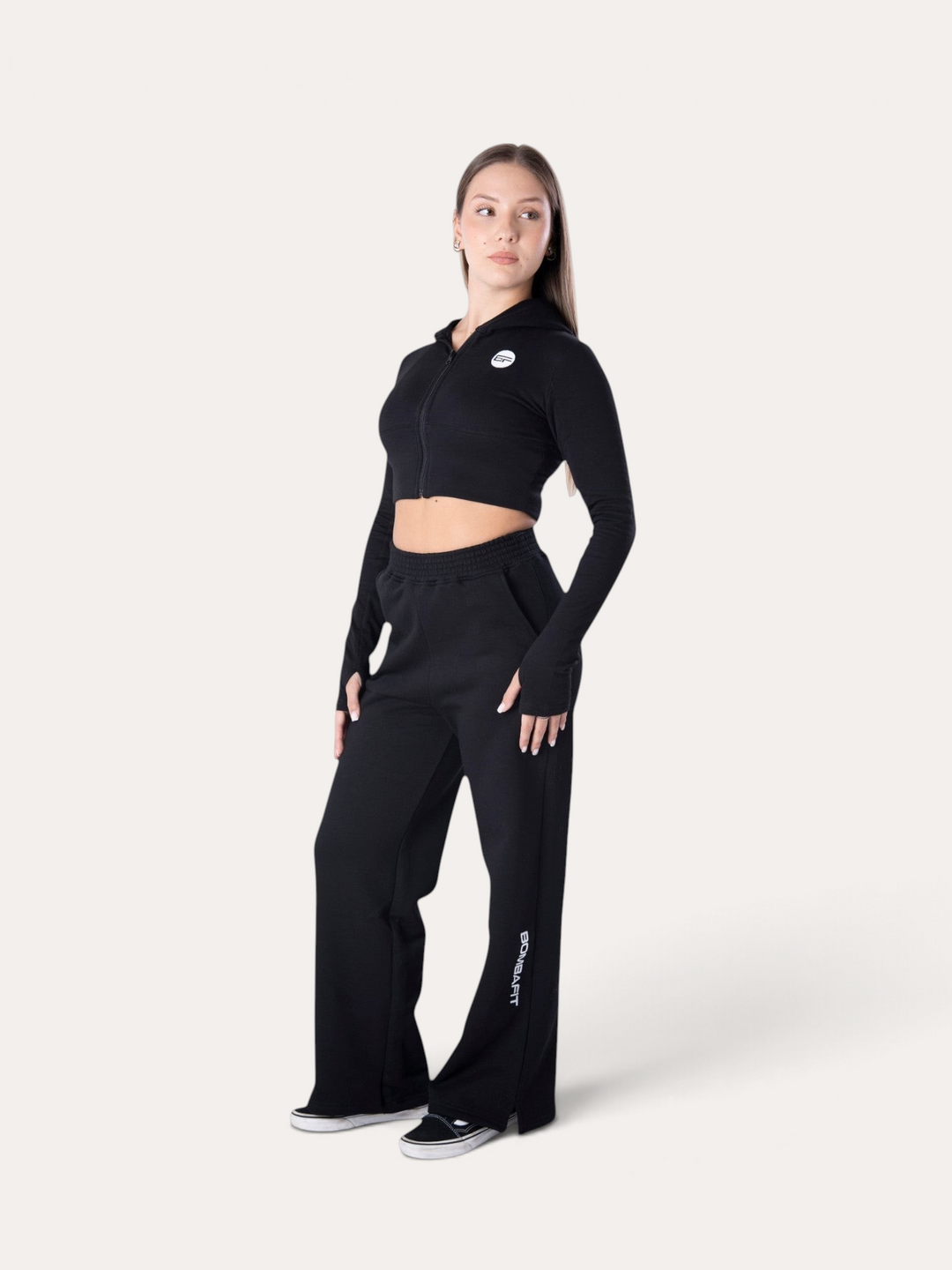 Modella indossa pantaloni della tuta neri Bombafit Flux con vestibilità ampia e logo laterale su sfondo neutro
