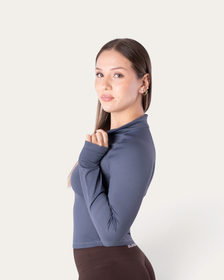 Modella indossa la giacca a maniche lunghe con zip Bombafit color acciaio, ideale per allenamento e fitness.