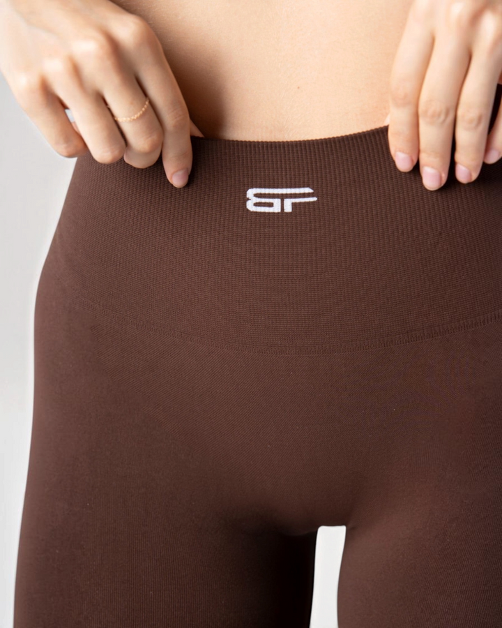 Dettaglio vita alta dei leggings Bombafit Arya Seamless marroni con logo bianco e tessuto tecnico traspirante