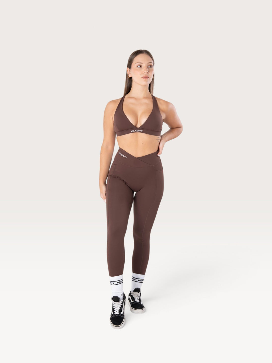 Modella indossa leggings Bombafit marroni a vita alta con dettaglio incrociato, tasche laterali ed effetto push-up