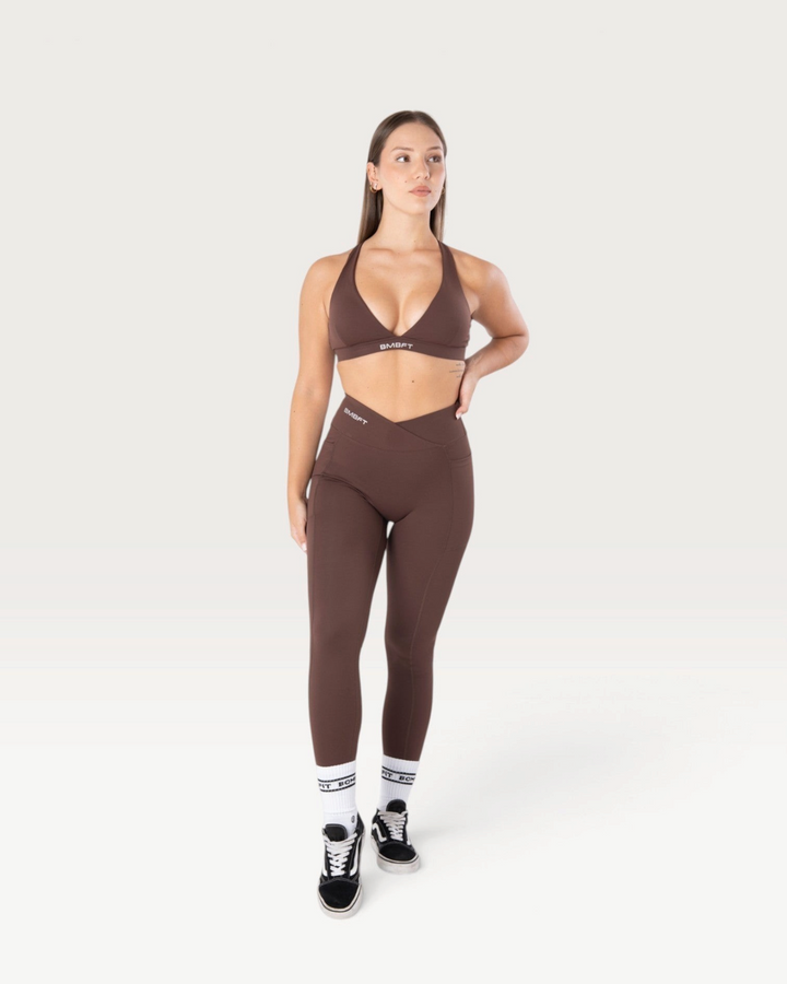 Modella indossa leggings Bombafit marroni a vita alta con dettaglio incrociato, tasche laterali ed effetto push-up