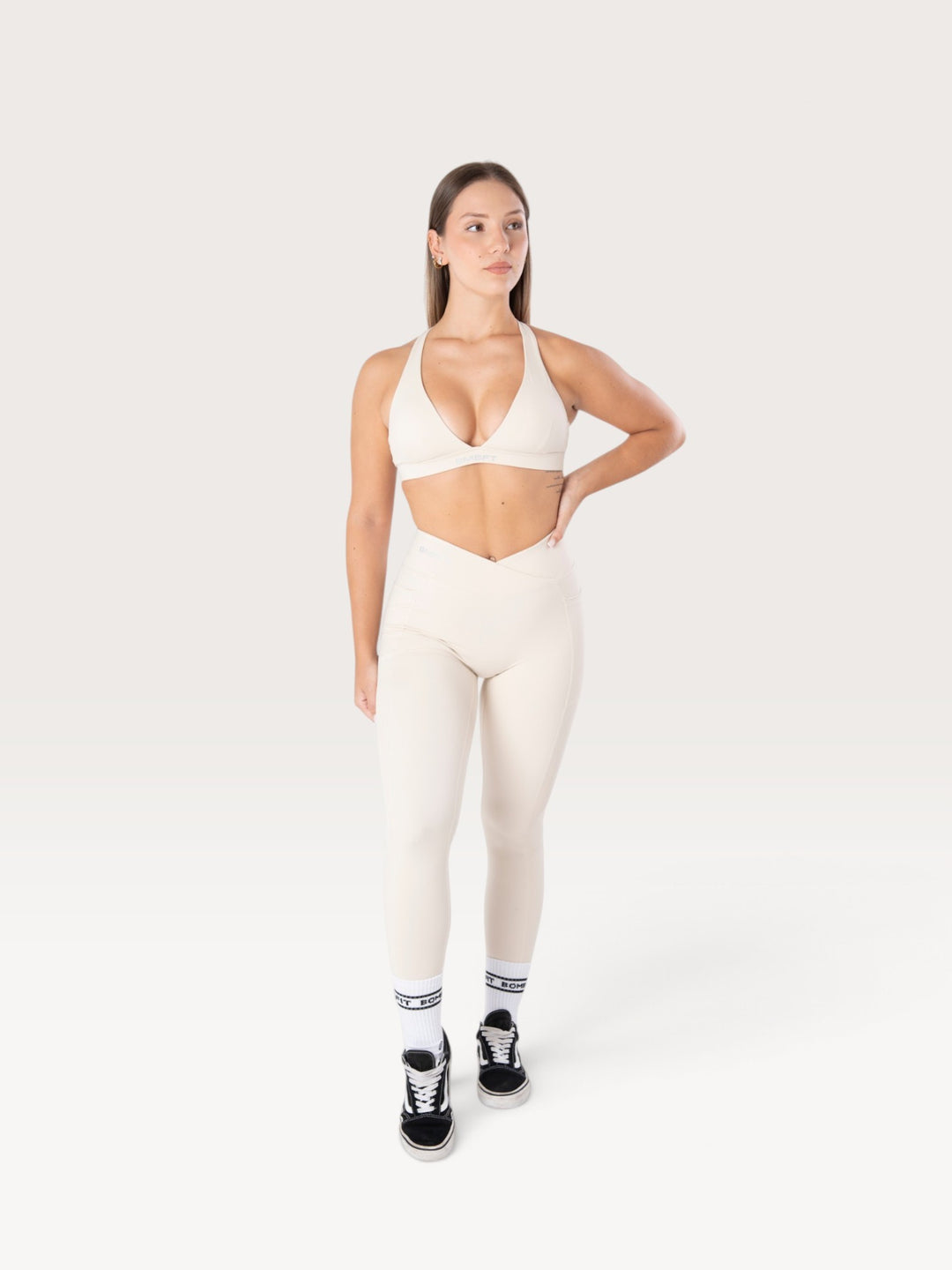 Modella indossa leggings Bombafit Sense beige a vita alta con incrocio frontale e tasche laterali per fitness