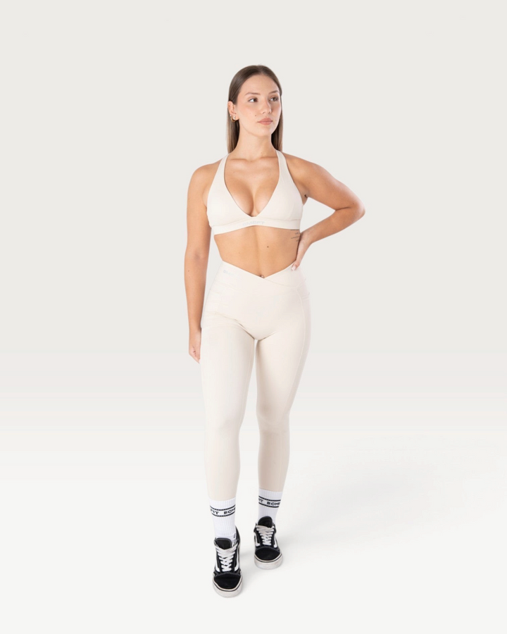 Modella indossa leggings Bombafit Sense beige a vita alta con incrocio frontale e tasche laterali per fitness