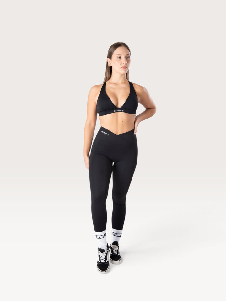 Modella indossa leggings Bombafit neri a vita alta con dettaglio incrociato, tasche laterali e effetto push-up.