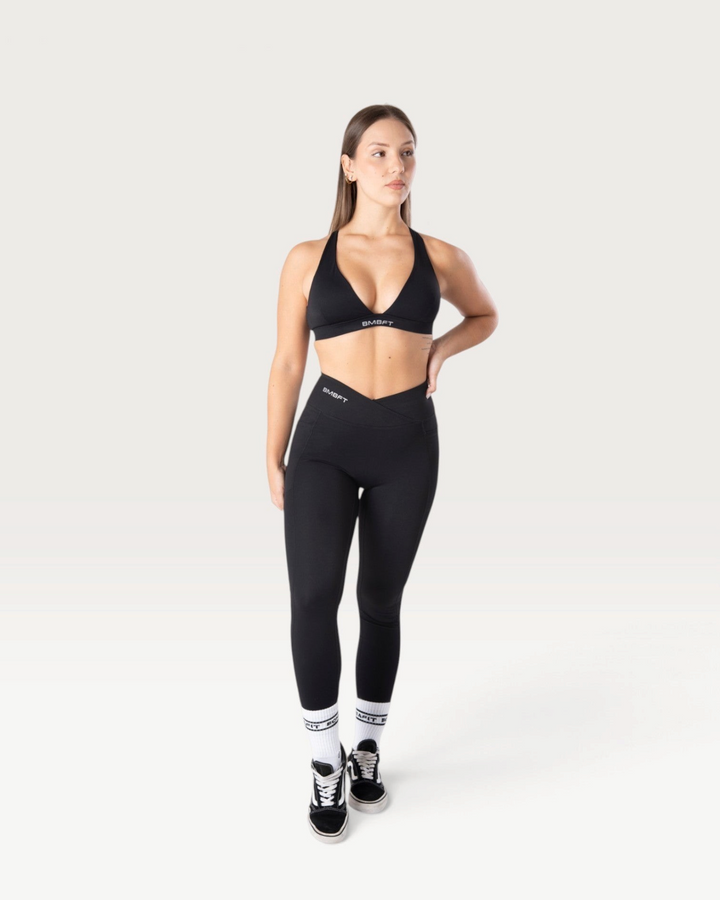 Modella indossa leggings Bombafit neri a vita alta con dettaglio incrociato, tasche laterali e effetto push-up.
