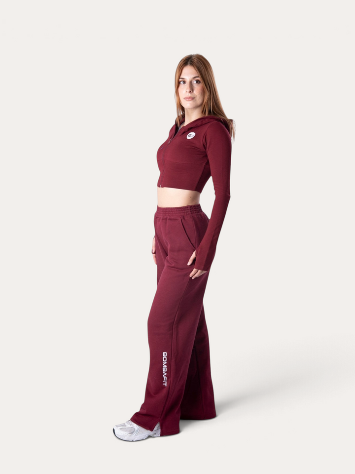 Modella indossa pantaloni della tuta Bombafit Flux color bordeaux con vestibilità ampia e logo laterale