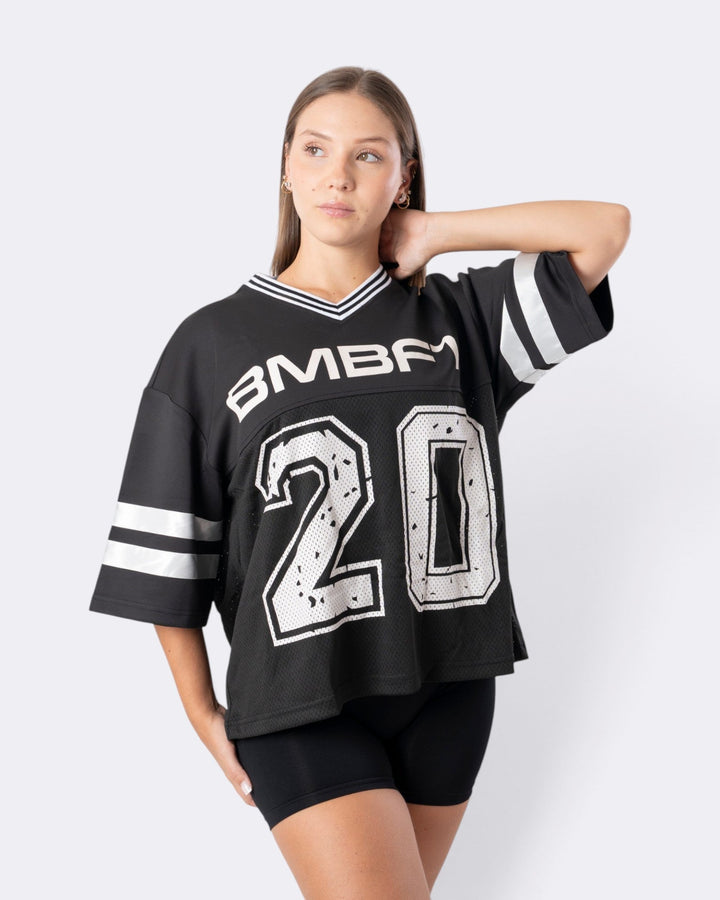 Modella indossa T-shirt oversize Bombafit nera stile basket con numero 20 bianco e scollo a V a righe