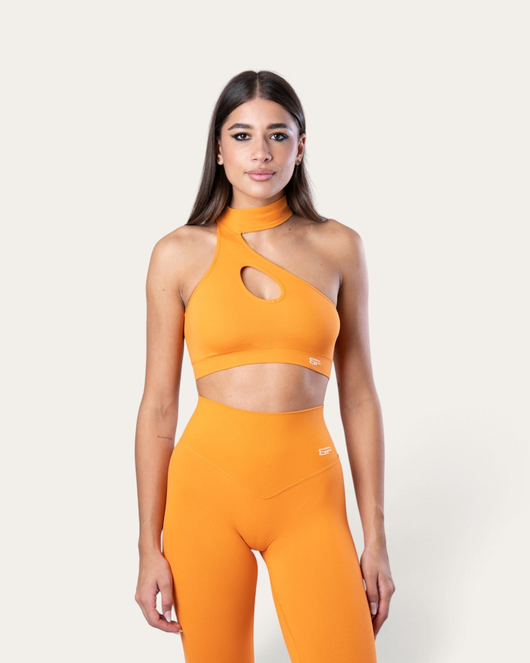 Modella indossa il top sportivo Bombafit Choker Seamless color arancione con design monospalla e dettaglio cut-out