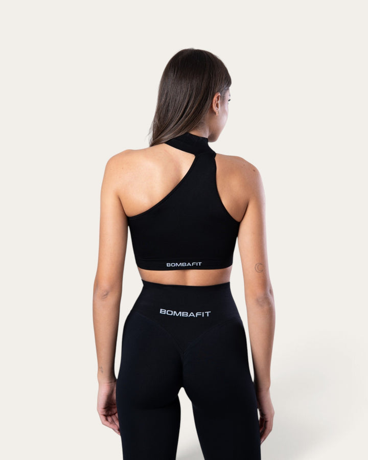 Modella di spalle indossa il top sportivo Bombafit Choker Seamless nero con design monospalla e scollo alto