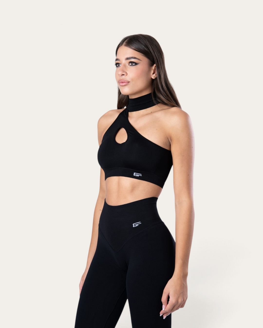 Modella indossa il top sportivo Bombafit Choker Seamless nero con scollo a goccia e design senza cuciture