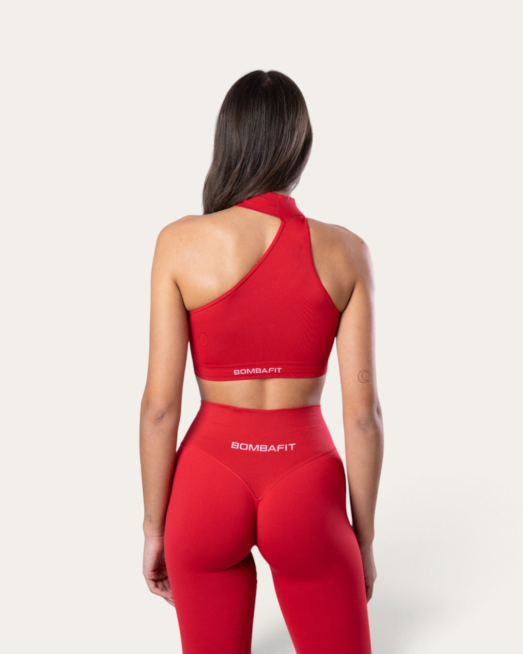 Vista posteriore di una modella che indossa il top sportivo choker seamless rosso sangue di Bombafit