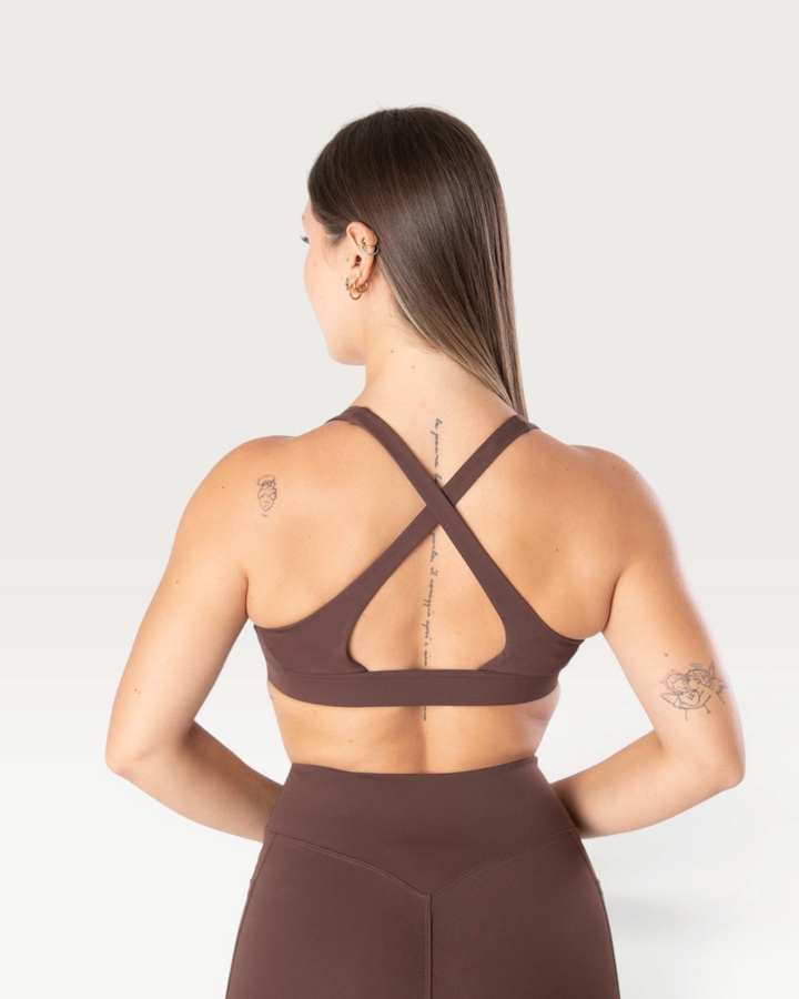 Modella indossa il top sportivo marrone Bombafit Sense con spalline incrociate sulla schiena e fascia sottoseno