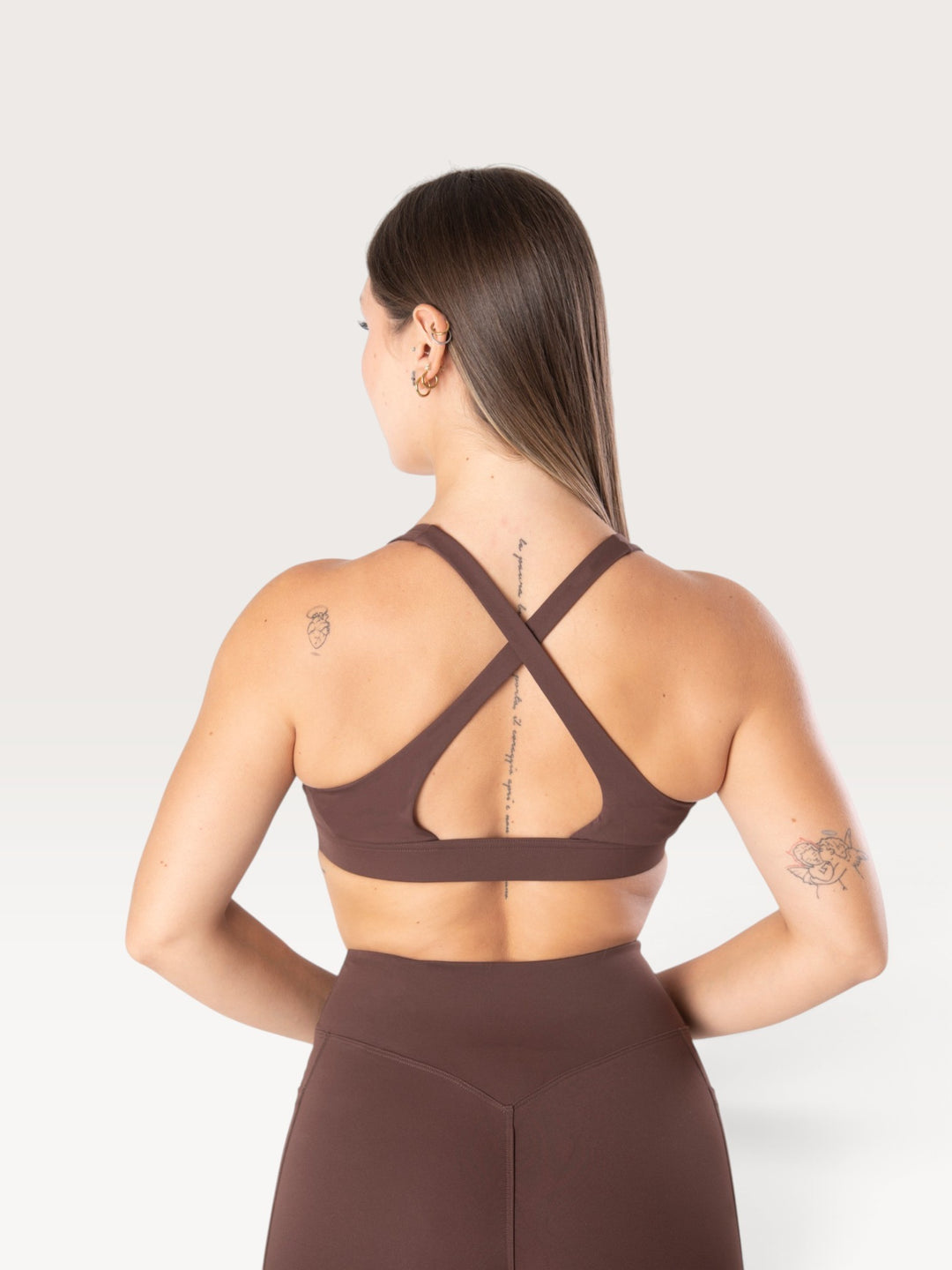 Modella indossa il top sportivo marrone Bombafit Sense con spalline incrociate sulla schiena e fascia sottoseno