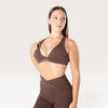 Modella indossa il top sportivo marrone Bombafit Sense con effetto push-up e logo BMBFT sulla fascia sottoseno