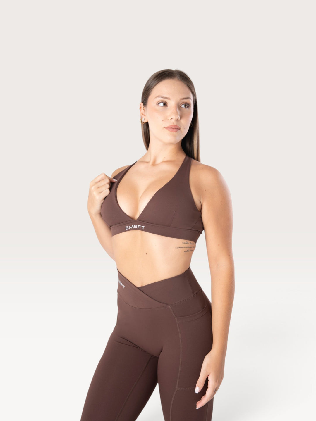 Modella indossa il top sportivo marrone Bombafit Sense con effetto push-up e logo BMBFT sulla fascia sottoseno