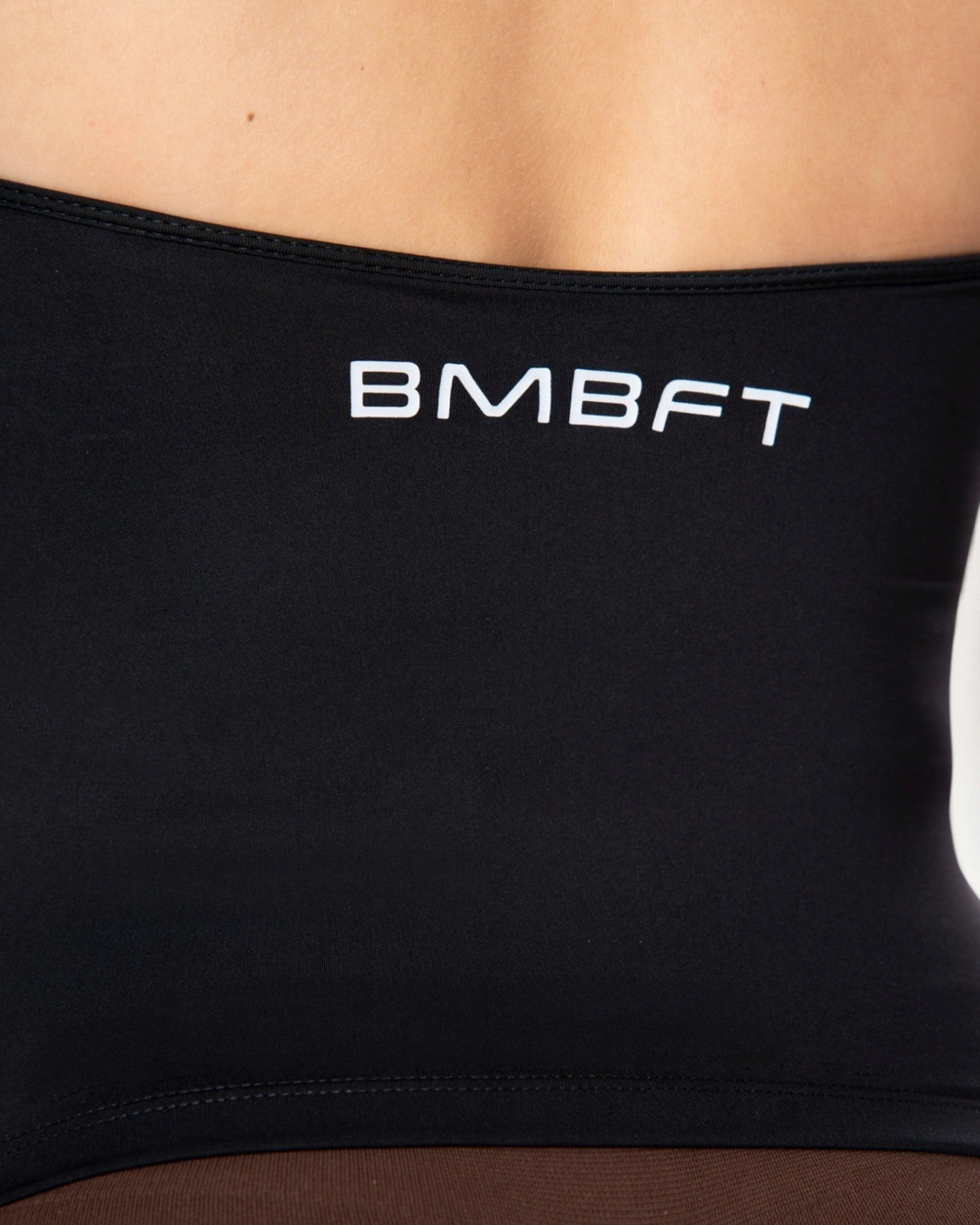 Dettaglio del top sportivo nero Bombafit con logo bianco stampato sul retro, realizzato in tessuto tecnico elastico.