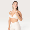 Modella indossa il top sportivo Bombafit Sense beige con spalline incrociate, effetto push-up e logo sottoseno