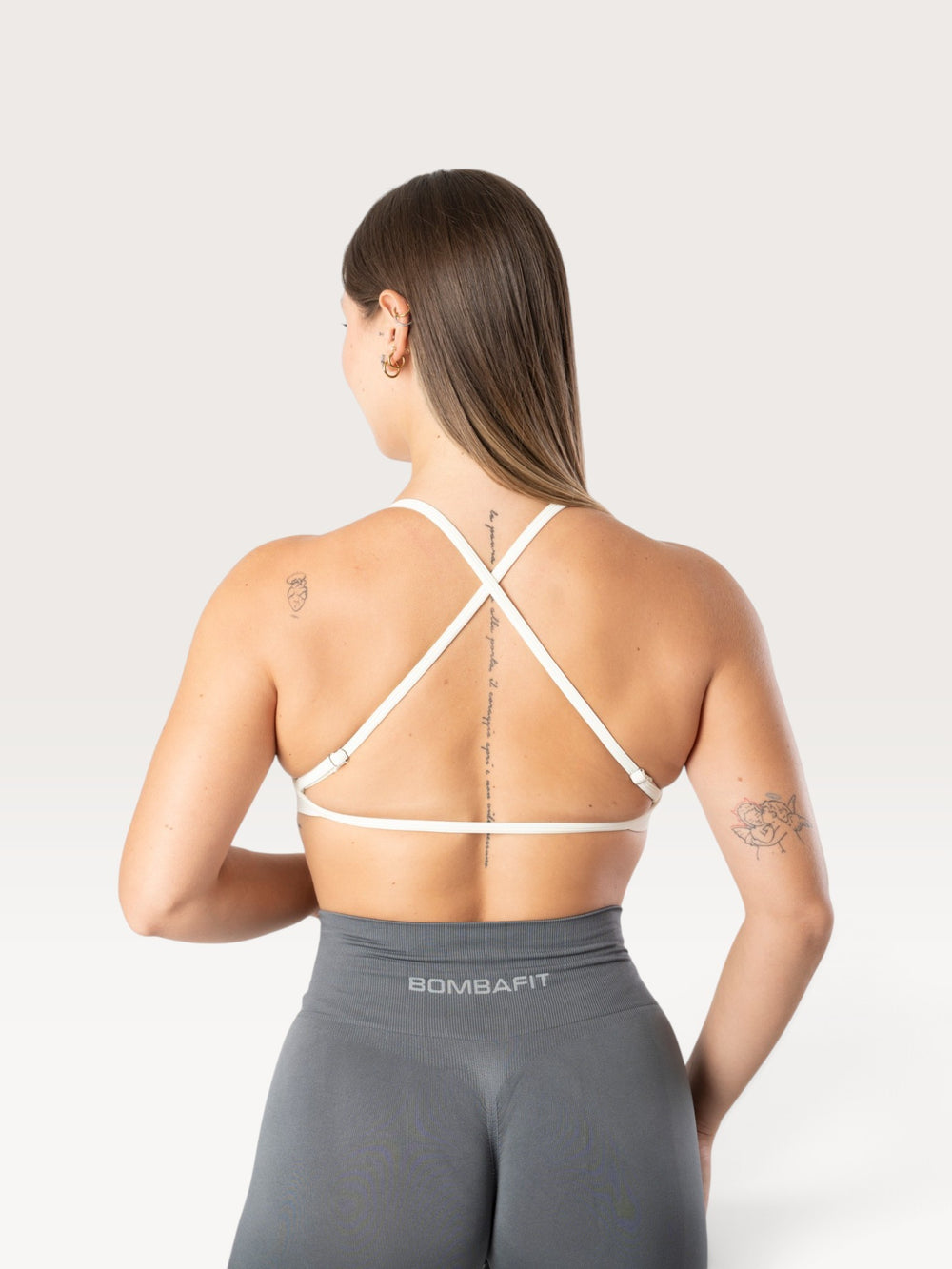 Modella di spalle indossa il top sportivo bianco Bombafit con spalline incrociate sulla schiena e tessuto seamless