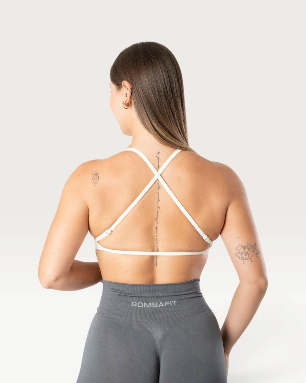 Modella di spalle indossa il top sportivo bianco Bombafit con spalline incrociate sulla schiena e tessuto seamless