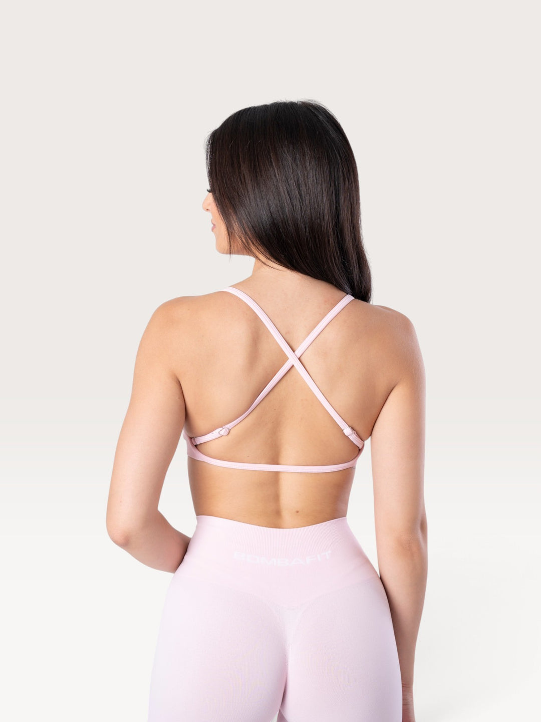 Modella di spalle indossa il top sportivo Bombafit Unity Seamless rosa fairy con spalline incrociate sulla schiena