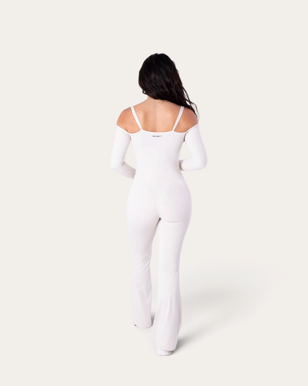 Modella di spalle indossa la tuta intera Diva Jumpsuit bianca di Bombafit con maniche lunghe e spalle scoperte