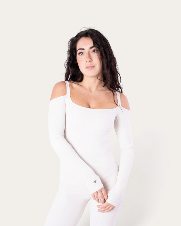 Modella indossa la tuta intera Bombafit Diva bianca a maniche lunghe con spalle scoperte e scollo rotondo