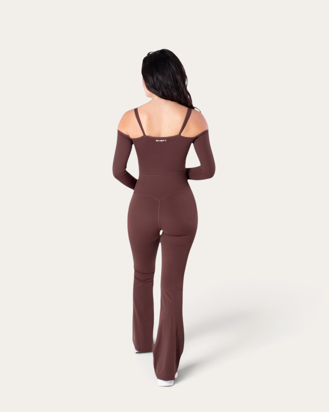 Modella di spalle indossa la tuta intera Diva Jumpsuit marrone di Bombafit con maniche lunghe e spalle scoperte