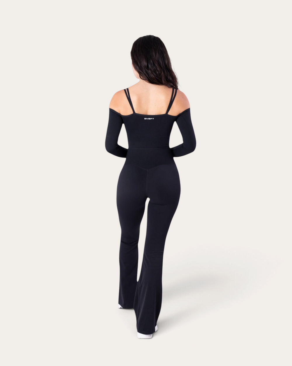 Modella di spalle indossa la tuta intera Diva Jumpsuit nera di Bombafit con maniche lunghe e spalline sottili
